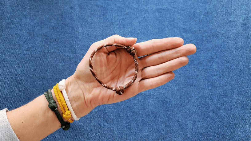 Woman wearing gree, gold and white paracord bracelets, and holding a football patterned paracord bracelet