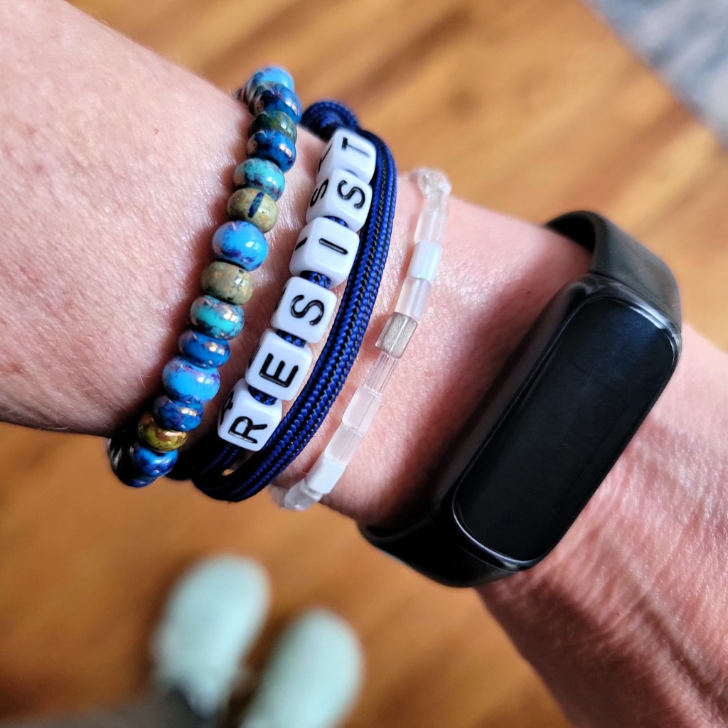 Close-up of a bracelet on a woman's wrist that has letter beads spelling out the word RESIST.