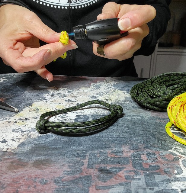 A woman's hand holding a paracord bracelet and a lighter being used to seal the ends of the bracelet.