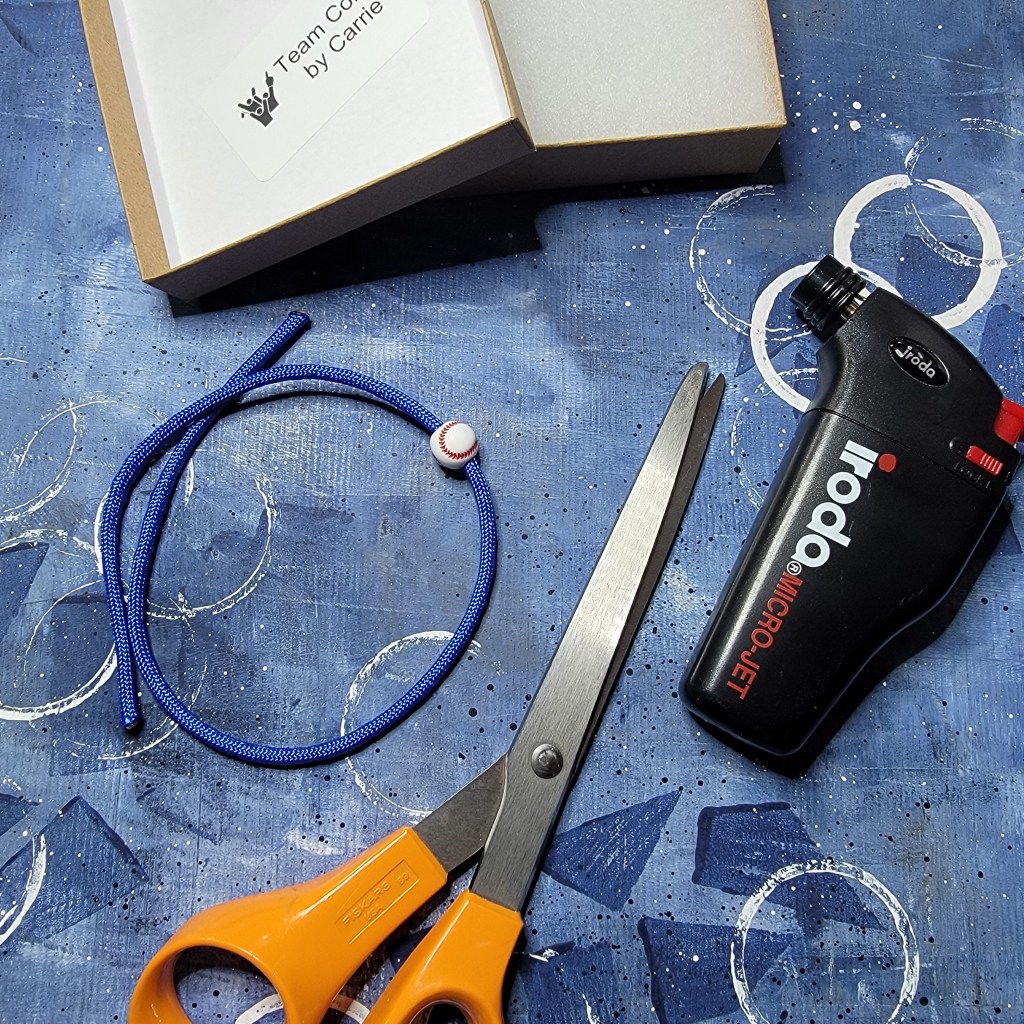 Tools and materials for making a royal blue paracord bracelet with a baseball bead.