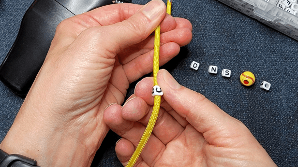 Close-up of hands threading beads onto paracord for a bracelet